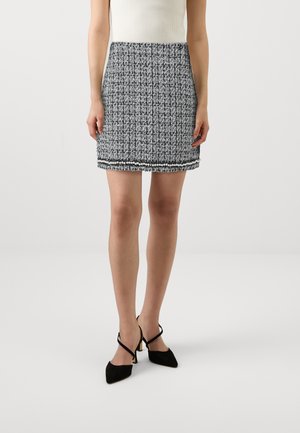 Jupe mini en tweed noir et blanc avec une surface texturée et un ourlet à franges, portée avec des talons aiguilles noirs à brides de cheville.