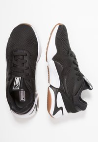 Schwarze Sportschuhe aus Mesh und synthetischem Leder, mit einem schwarzen Schnürsystem, weißer Sohle und braunen Sohlelementen.