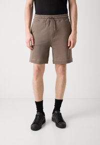 Shorts en coton beige clair avec taille élastique, cordon de serrage et poches latérales, associés à des baskets noires et des chaussettes mi-mollet.