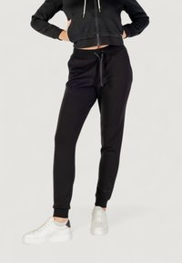 Czarna bluza z zamkiem błyskawicznym o strukturalnym wzorze, zestawiona z dopasowanymi czarnymi spodniami dresowymi, dopełniona białymi sneakersami z czarnym akcentem.