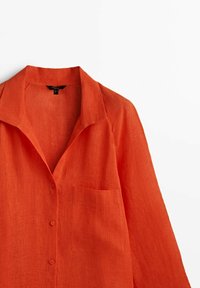 Långärmad orange linneskjorta med krage, framficka på vänster sida och tre knappar fram.