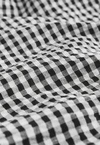 Tissu à carreaux noir et blanc avec un motif de petits carrés, présenté en gros plan avec une texture visible et de légers plis.