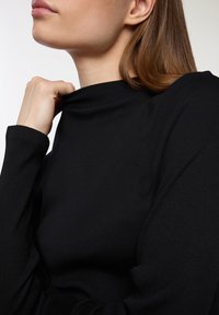 Czarna, prążkowana bluzka z długim rękawem i wysokim kołnierzem. Zbliżenie na teksturowany materiał oraz dopasowanie wokół szyi i ramion.