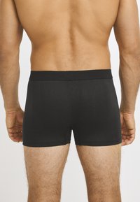 Black boxer briefs made of soft fabric with an elastic waistband, featuring a fitted design and smooth texture. Back view shows leg openings.