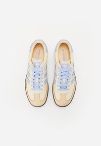 Ett par beige och ljusblå Adidas-sneakers med snörning, vytt från ovan på vit bakgrund.