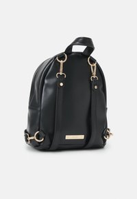 Mochila de cuero sintético negro con herrajes dorados, forma redondeada, asa superior y correas ajustables. Cuenta con una placa metálica con la marca.