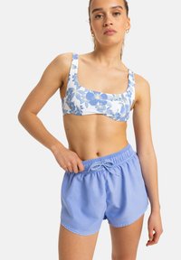 Bikini-Oberteil mit Blumenmuster in Weiß und Blau, kombiniert mit hellblauen Shorts mit Kordelzug, elastischem Bund und glatter Baumwolloberfläche.
