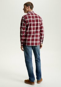 Camicia di flanella a scacchi rossi e bianchi con maniche lunghe, polsini con bottoni e colletto, indossata con jeans blu e scarpe marroni.