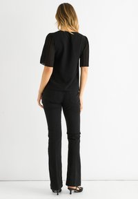 Black blouse with short pleated sheer sleeves, round neck, and smooth fabric; paired with black flared jeans and high-heeled shoes.