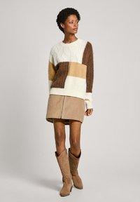 Adīta džemperis ar kabelīšu rakstiem krēmkrāsā, brūnā un dzeltenīgā krāsā. Saskaņota ar brūnu korduru svārku un bēšiem kaubojiem zābakiem.