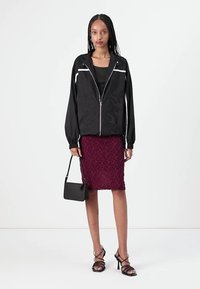 Black zip-up jacket with flame pattern, paired with a burgundy textured pencil skirt. Model carries a small black handbag and wears strappy heels.