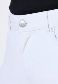 Jeans bianchi in cotone con un classico design a cinque tasche, un bottone argentato con dettaglio del logo e cuciture visibili lungo le cuciture.