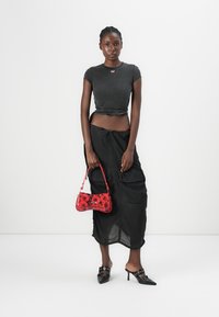 T-shirt noir court avec un logo rouge, jupe longue transparente noire, sac à main à motif floral rouge, chaussures à talons hauts noires avec lanières.