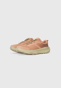 Baskets de course rose clair avec un tissu texturé, bout renforcé, semelle intermédiaire beige et accents jaunes sur les lacets. Présente le logo Vibram sur la semelle extérieure.