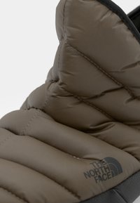 Flaffete, beige-brun sovepose med kviltede sektioner. Har et logo i mørkegrå nederst, blød tekstur og et slankt design.