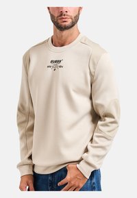 Felpa beige con scollo a coste, logo ricamato e maniche a contrasto con texture diversa. Tessuto morbido con vestibilità casual e design minimalista.