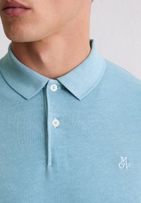 Lichtblauw poloshirt van katoen. Uitgerust met een klassieke kraag, een knoopsluiting met drie knopen en een geborduurd "MOP"-logo in wit. Soepele textuur.