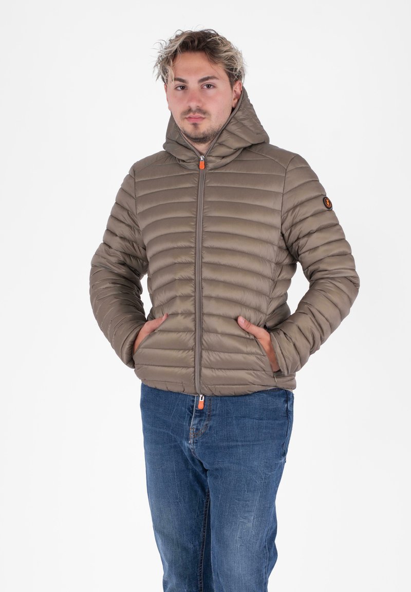Gevoerde khaki jas met capuchon, voorzien van horizontale gestikte lijnen, een voorste ritsluiting met oranjeaccent en zijzakken.