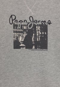 Tela gris con un gráfico negro de una persona en una escena urbana nocturna, superpuesto con el texto "Pepe Jeans" y un pequeño eslogan de la marca debajo.