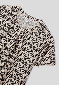 Blusa nera con motivo a foglie su uno sfondo beige chiaro, dotata di scollatura a V e maniche corte, con una texture di tessuto morbida e liscia.