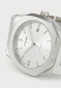 Montre automatique en acier inoxydable avec un boîtier octogonal, un cadran argenté, des repères minimalistes et une fenêtre de date positionnée à trois heures.