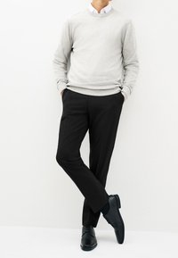 Maglione grigio chiaro, pantaloni neri e scarpe eleganti nere. Il maglione ha una scollatura rotonda; i pantaloni sono a taglio dritto con tasche laterali.