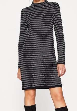 Zwart-wit horizontaal gestreepte jurk met lange mouwen en een hoge hals, gedragen met zwarte kniehoge laarzen.
