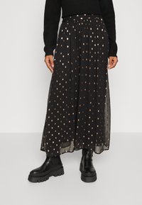 Svart plisserad kjol med ett mönster av guldprickar, tillverkad av lättviktsmaterial. Stylad med kraftiga svarta ankellånga stövlar.