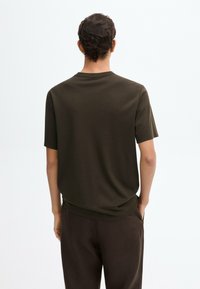 T-shirt a maniche corte verde oliva, realizzata in tessuto morbido, con taglio dritto e scollatura rotonda, vista da dietro. Design minimalista.