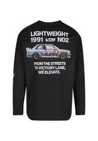 Juodas ilgomis rankovėmis marškinėliai su spalvinga lenktyninio automobilio grafika. Tekstas ant nugaros skaitomas: "LIGHTWEIGHT 1991 UTM NO2 NUO GATVIŲ IKI PERGALĖS LINIJOS, MES KELIAME."