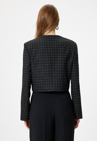 Blazer crop nero con motivo a griglia bianca; presenta maniche lunghe e un design dritto sul retro. Tessuto morbido; costruzione minimalista.