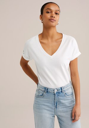 Vit V-ringad T-shirt med uppvikta ärmar, tillverkad av mjukt tyg; i kombination med ljusblå högmidjade jeans med klassisk knäppning.