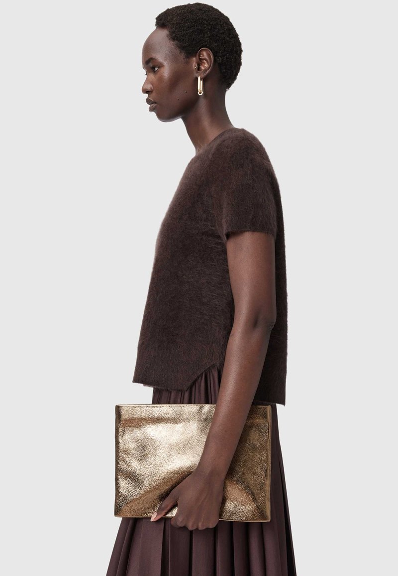 Brun stickad kortärmad tröja med luddig yta kombinerad med en plisserad brun kjol. Modellen håller en glänsande gyllene metallickuvertväska.