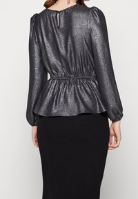 Metallisch graues Peplum-Oberteil mit langen Puffärmeln, elastischem Taillenbund und einer Schlüssellochöffnung auf der Rückseite. Glatte Textur mit glänzendem Finish.