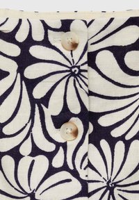 Tessuto bianco con motivo floreale blu scuro, con dettagli in crema sui bottoni. Il design include grandi fiori stilizzati e linee curve.