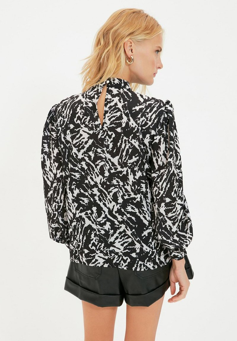 Czarna i biała bluzka w wzory z wysoką szyją, bufiastymi rękawami oraz wycięciem w kształcie klucza z tyłu, zestawiona z czarnymi skórzanymi szortami.