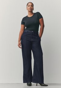 Top negru mulat cu mâneci scurte, asortat cu pantaloni evazați din denim închis, cu talie înaltă. Pantofii cu toc completează ținuta, accentuând silueta.