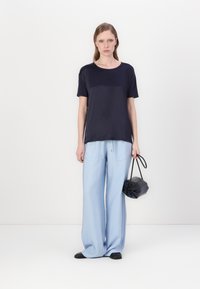 Camicia a maniche corte navy abbinata a pantaloni a gamba larga blu chiaro. Le scarpe con tacco basso nere e una piccola borsa nera completano il look.