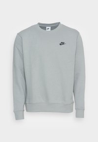 Ljusgrå Nike-tröja med långa ärmar, ribbade manschetter och rund hals. Har en liten svart logotyp på bröstet. Tillverkad av mjukt material.