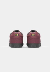 Maroon suede skate shoes with black rubber soles, rounded toe, padded collar, and logo detailing in yellow on the back.