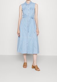 Jasnoniebieska sukienka koszulowa z denimu z zapięciem na guziki, kołnierzykiem i regulowanym paskiem. Połączona z brązowymi plecionymi sandałami na słupku.