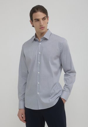 Camicia a maniche lunghe azzurra pallido con un motivo sottile, vestibilità su misura e colletto a bottoni. Il materiale sembra liscio con una leggera lucentezza.