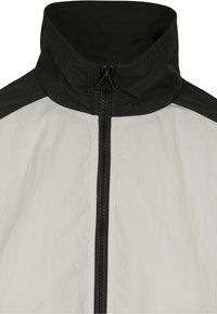 Lättviktsjacka med svart krage och axlar, med en hel svart dragkedja fram och en texturerad vit kropp.