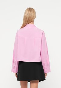 Ρο ζ κοντομάνικο πουκάμισο με γιακά, μακριά μανίκια και διακοσμητικά κουμπιά, με πιετά στο πίσω μέρος και λεία υφή υφάσματος. Μαύρη φούστα.