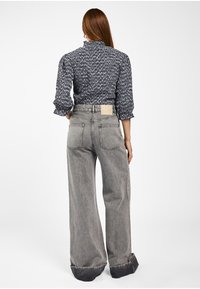 Grijze wijde jeans met een hoge taille, met een zichtbare label aan de achterkant en stikseldetails. Het materiaal lijkt denimachtig met een lichte textuur.