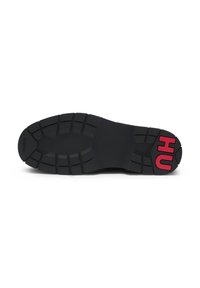Suela de zapato negra con surcos profundos para tracción, con letras rojas "HU" cerca del talón y el texto "HUGO" cerca de la puntera.