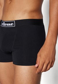 Schwarze Boxer Shorts aus weichem Material mit einem elastischen Bund, auf dem der Markenname "ellesse" in weißer Schrift aufgedruckt ist.