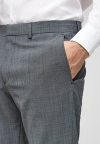 Grijze geruite broek met een gladde textuur, voorzien van zijzakken en een tailleband. De stof toont een subtiel patroon van kleine vierkantjes.