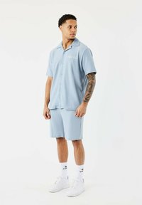 Camisa de manga corta azul claro y pantalones cortos a juego en una tela texturizada con cuello, combinados con zapatillas blancas y calcetines cortos.