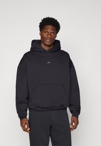Sudadera negra hecha de un tejido suave, con una gran capucha, un bolsillo frontal y un pequeño logo en el pecho. Corte relajado con puños de canalé.
